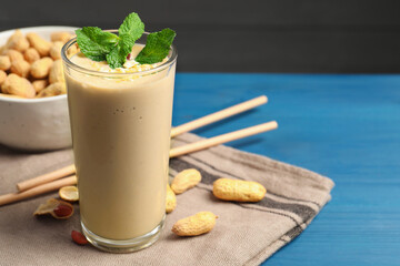 Glass of tasty banana smoothie with peanuts and mint on light blue wooden table, closeup. Space for text