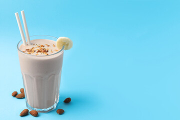 Glass of tasty banana smoothie with straws and almond on light blue background. Space for text
