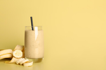 Glass of tasty smoothie with straw and cut banana on pale yellow background. Space for text