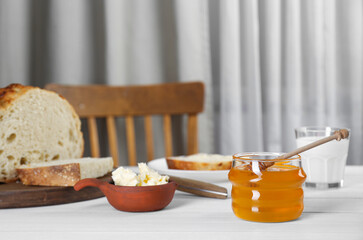Jar with honey, butter, bread and milk served for breakfast on white wooden table