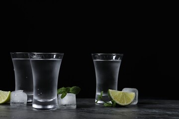 Shot glasses of vodka with lime slices, ice and mint on grey table