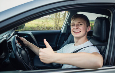 Happy and proud guy shows thumb up gesture. Confident driver with fasten belt behind steering wheel