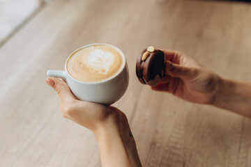 Woman hands holding cup of coffee with french sweets. Top view shot of female having hot beverage with latte art foam and macaroon dessert cake. Close up, copy space, background.