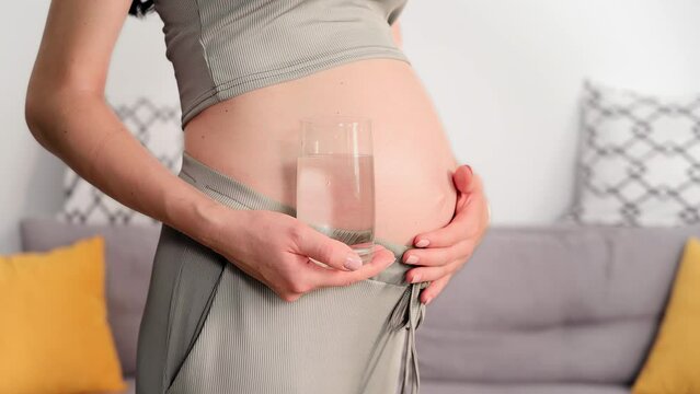 water balance, a loving woman strokes her belly with hand and holds a glass glass with clean healthy water, close-up