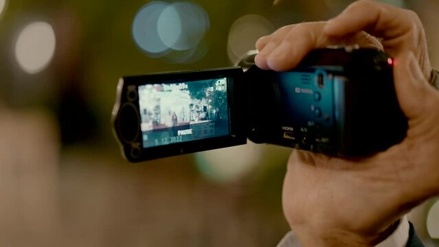 Close-up shot of an adult man's hand taking a video with a small video camera and pressing pause. stares at the screen of a camera.