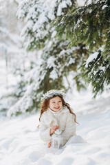 A little girl is sitting in a snowy park. Winter magic