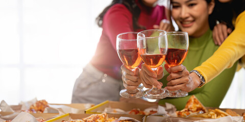 Group of Asian friends gather to celebrate Christmas with champagne and eating pizza at home. Joy of holiday party with friends or colleague concept