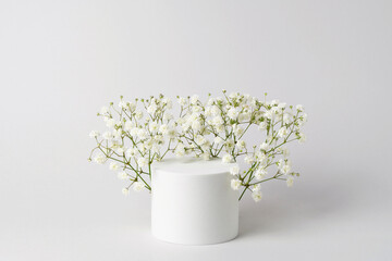 Empty white round podium and gypsophila flowers on light grey background. Showcase for product sale...