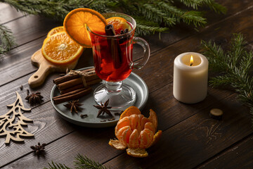 Christmas mulled wine and tangerines on a wooden table. Fir branches and a candle create a holiday...