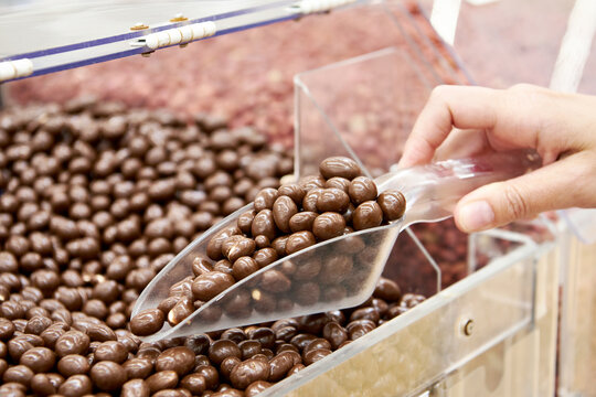 Hand with scoop dragee in chocolate glaze in shop