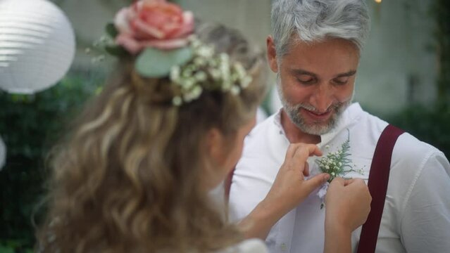 Mature groom recieving decoration on his shirt from bride at wedding reception outside in the backyard.
