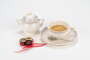 Set of antique porcelain coffee cup with sugar bowl and delicious chocolate candies tied with a red ribbon on a white background