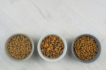 Dry food for cats and dogs in bowls on a white wooden background. Top view.