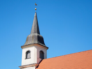 Close up view to church tower with golden rooster on the top against clean blue sky.