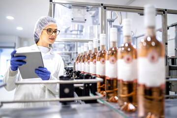 Female factory technologist controlling wine production in alcohol beverage bottling plant.