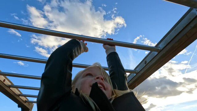 5 years old caucasian girl is hanging monkey bar at the playground with happiness and enjoyment during daytime