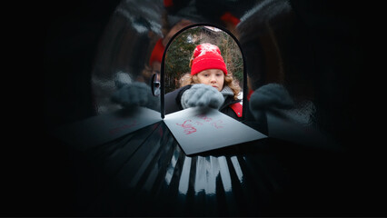 POV Cute little kid boy puts a letter with his Christmas wishes addressed to Santa Claus, Notrh Pole into the mailbox