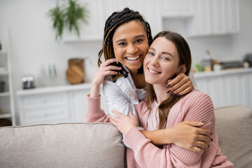 positive african american lesbian woman hugging joyful girlfriend in living room.