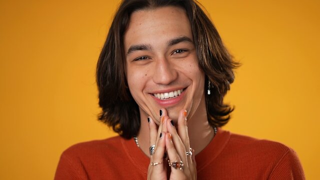 Portrait of happy handsome gender fluid Latino Hispanic non-binary young man 20s wearing orange casual shirt isolated on yellow color background in studio.