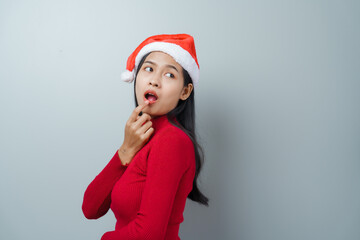 Pretty lovely lady asian thai women in red sweater and santa christmas hat isolated over grey background. thinking and surprise