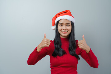 Pretty lovely lady asian thai women in red sweater and santa christmas hat isolated over grey background. thumb up