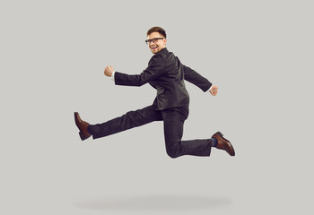 Fototapeta na wymiar Young positive Caucasian man jumping and smiling broadly rejoicing in success in business or career as manager hanging in air in pose of runner dressed in trousers and jacket on studio background