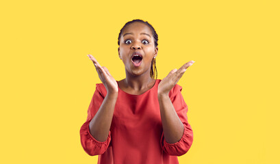 Happy excited emotional dark-skinned young woman raises her hands rejoicing isolated on yellow...