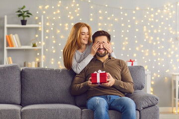 Secret gift. Cute red-haired woman closes her boyfriend's eyes with her hands and gives him a...