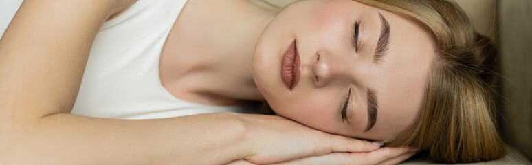 Young and blonde woman with closed eyes sleeping on sofa at home, banner.