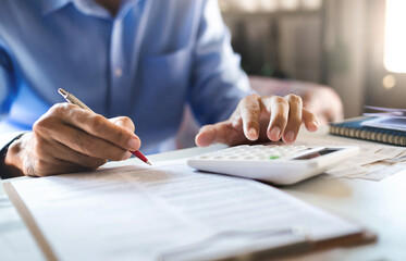 Asian businessman on desk in office holding pen and using calculator to calculate expenses with...