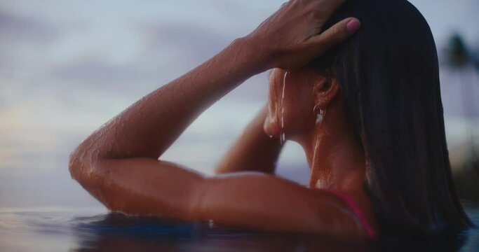 Close up of beautiful woman emerging from the water of luxury resort pool at sunset, relaxing health and wellness spa vacation