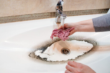 a woman wets a rag, squeezes and washes the sink in the bathroom.