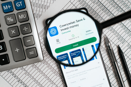 Cowrywise saving and investing money mobile application in online store on smartphone screen at workplace. Top view, close-up, view through magnifying glass. Astana, Kazakhstan 12.12.2022