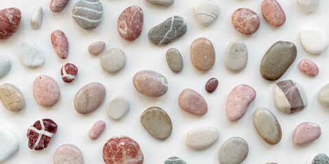 Top view close up sea stones on light background. Colorful pebbles as summer pattern. Natural stone white red pink grey colors. Minimal flat lay, banner with natural materials