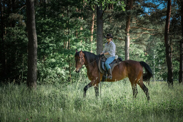 Portrait of a young beautiful girl in a cowboy hat on a horse in the forest.