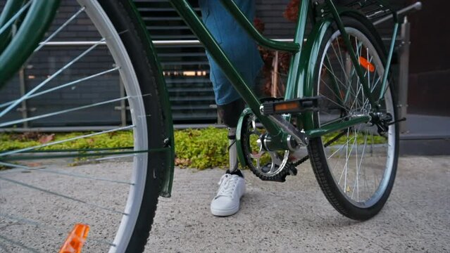 Slow motion view of a man with prosthetic legs. Getting on his bike and driving away