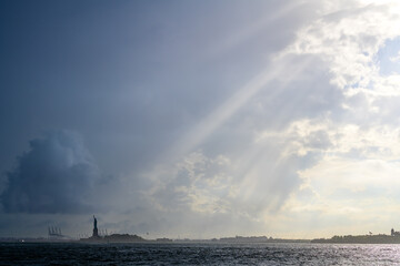 Fototapeta na wymiar The Statue of Liberty lighten by sun rays in a cloudy day in New York City.