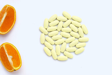 Vitamin c pills with orange fruit on white background.
