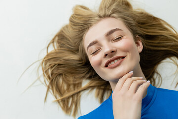 Fototapeta premium top view of happy blonde woman lying and touching chin on grey background.