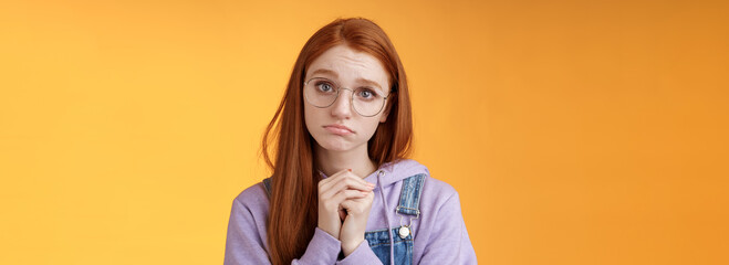 Pretty please. Clingy young sad sulking redhead girl sibling wearing glasses pouting silly press palms begging gesture pleading wanna receive help promise be good ask favour, orange background - obrazy, fototapety, plakaty