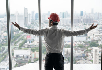 Handsome caucasian engineer man  with hardhat looking to the city outside window