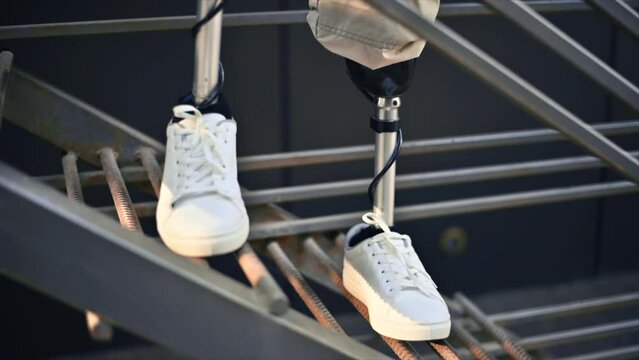 Slow motion view of a man with prosthetic legs and white sneakers staying on a metal staircase