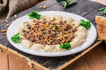 Hummus with meat and pine nuts served in dish isolated on table side view of arabic food