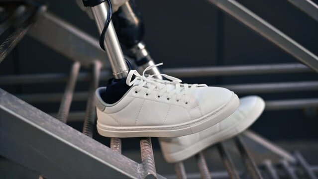 Slow motion view of a man with prosthetic legs and white sneakers sitting on a metal staircase