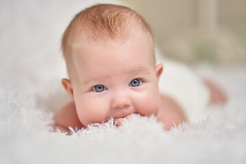 portrait of an infant lying on its stomach on a soft comforter looking at the camera smiling