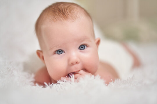 portrait of an infant lying on its stomach on a soft comforter looking at the camera smiling