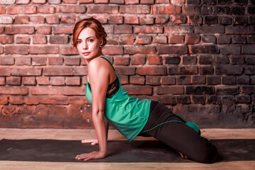 Fototapeta na wymiar A young slender girl in black leggings and a birch T-shirt sits in an asana against the background of a brick wall.