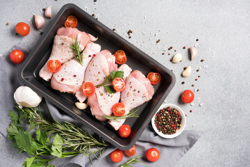 Raw chicken legs in black baking form with seasonings and tomatoes over gray concrete background. Chicken drumsticks ready to cook. Organic meat, healthy eating concept