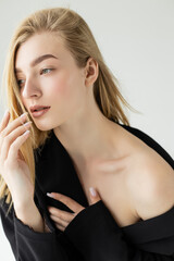 Obraz premium portrait of young blonde woman with naked shoulder posing with hand near face isolated on grey.