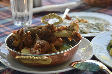 Goat meat cooked in tandoor served on copper pan on a garden table. Close-up of lamb meat tandoori . Traditional Aegean, Turkish kitchen.